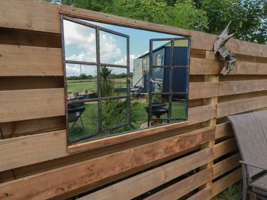 A wooden fence with a window mirror reflecting a garden and outdoor furniture at Dot May in Porteath near Polzeath
