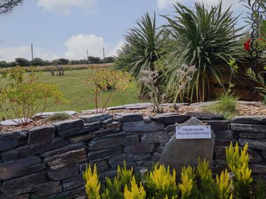 A garden with stone wall plants and a sign that says trespassers will be composted at Dot May in Porteath near Polzeath