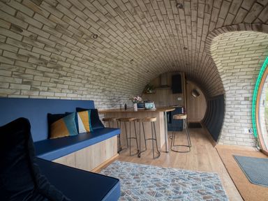 An arched brick room with a blue bench with cushions a wooden kitchen island with stools and a round door at Badgers View in Rhayader