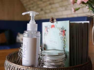 A table with a bottle of hand cleanser a jar with a latch and a guest book with a floral design at Badgers View in Rhayader