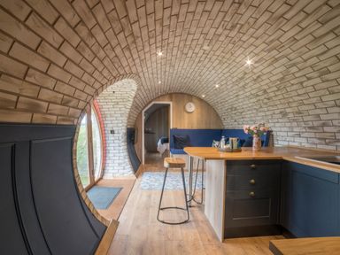 An arched room with wooden flooring a kitchen area with stools and a seating area with cushions at Badgers View in Rhayader