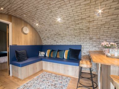 A corner seating area with blue cushions and pillows next to a wooden breakfast bar with stools at Badgers View in Rhayader