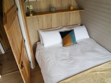 A bedroom with a white bed with pillows a wooden shelf with a lamp clock and candle a wooden door at Badgers View in Rhayader