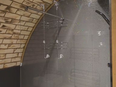 A shower area with a glass partition and a metal hanging caddy at Badgers View in Rhayader