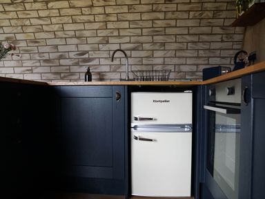 A kitchen with a small white Montpellier fridge a sink and faucet dark cabinets and a built in oven at Badgers View in Rhayader