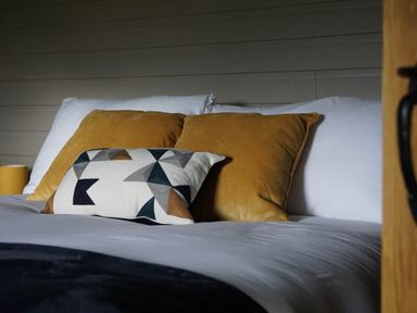 A bed with white sheets two yellow pillows and one patterned cushion at Badgers View in Rhayader