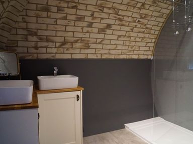 A bathroom with two white sinks on wooden countertops a brick arched wall and a shower area at Badgers View in Rhayader
