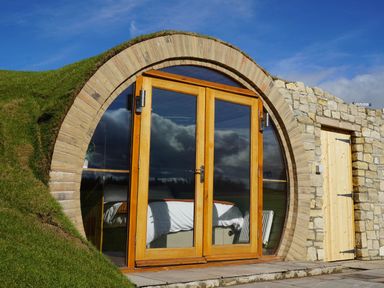 A circular wooden door with glass panels built into a grassy hillside at Hares View in Rhayader
