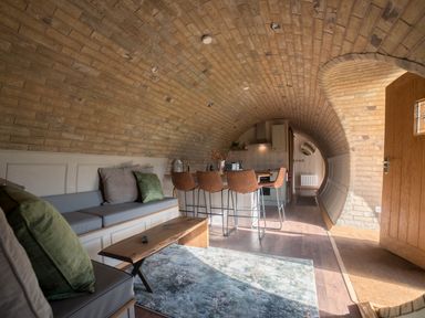 A curved brick interior with a seating area a wooden coffee table chairs and a kitchen at Hares View in Rhayader