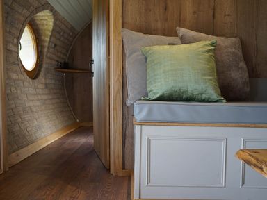 A small seating area with cushions beside a doorway in a wooden interior with a round window at Hares View in Rhayader