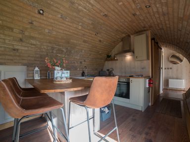 A kitchen area with a wooden island and brown chairs under a curved brick ceiling at Hares View in Rhayader