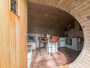 A kitchen with an arched brick ceiling a wooden dining table two brown chairs and built in cabinets at Hares View in Rhayader