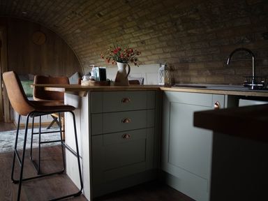A kitchen with a wooden countertop stools a sink flowers on the counter and a clock on the wall at Hares View in Rhayader