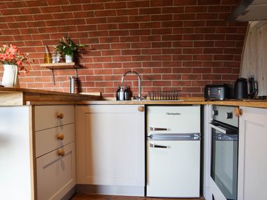 A kitchen with wooden countertops white cabinets a brick wall a white Montpellier fridge a black toaster and kettle at Hares View in Rhayader