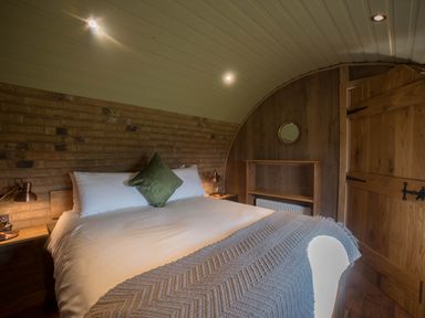 A bedroom with a bed a green pillow a knitted blanket bedside tables with lamps a small shelf and a wooden door at Hares View in Rhayader