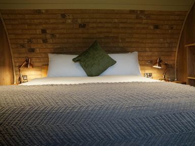 A bed with white pillows and a green cushion with wall lamps on each side at Hares View in Rhayader