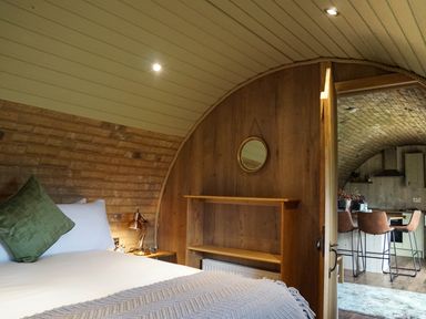 A bedroom with a bed and green pillow next to a door leading to a kitchen with bar stools at Hares View in Rhayader