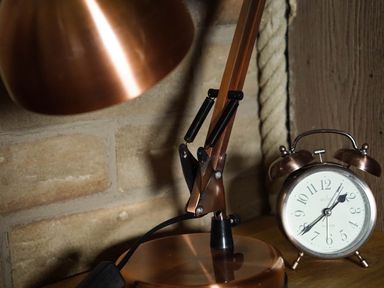 A copper desk lamp and a copper alarm clock on a wooden surface against a brick wall at Hares View in Rhayader