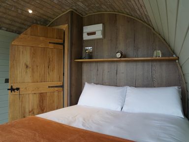 A bedroom with a bed with white pillows and a brown blanket a wooden door and a wooden shelf with an alarm clock and a lamp at Hares View in Rhayader