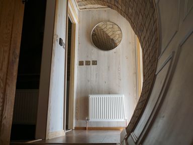 A hallway with a wooden floor radiator and a round mirror on the wall at Hares View in Rhayader