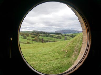 A circular window view of green fields trees hills and cloudy sky at Hares View in Rhayader