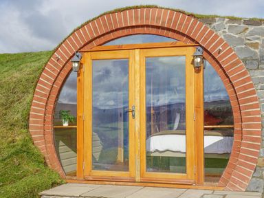 A round brick entrance with wooden framed glass doors showing a bed and plant inside at Hares View in Rhayader