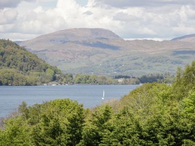 A lake with a sailboat surrounded by trees and hills in the background at Gosling Cottage Kendal