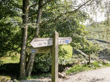 A wooden signpost on a trail showing directions to Grasmere and Ambleside with trees and grassy fields in the background