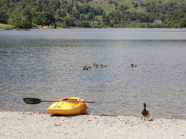 A yellow kayak on a pebbled shore near ducks swimming in a lake with hills in the background at Gosling Cottage Kendal
