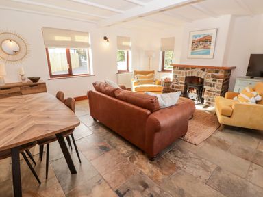 A living room with a brown sofa yellow armchairs a wooden dining table and a stone fireplace at Fountain Folly in Moylgrove near St Dogmaels