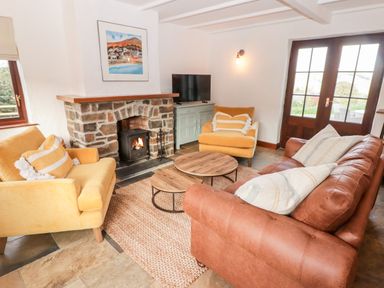 A living room with a stone fireplace two yellow armchairs a brown sofa a rug and a TV cabinet at Fountain Folly in Moylgrove near St Dogmaels