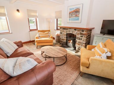 A living room with a brown sofa yellow armchairs stone fireplace and round wooden coffee tables at Fountain Folly in Moylgrove near St Dogmaels