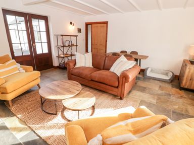 A living room with two yellow armchairs a brown leather sofa wooden coffee tables a shelf and a dog bed at Fountain Folly Moylgrove near St Dogmaels