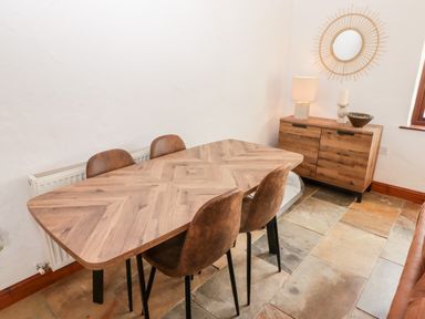 A dining area with a wooden table and four chairs next to a wooden sideboard with a lamp and mirror at Fountain Folly in Moylgrove near St Dogmaels