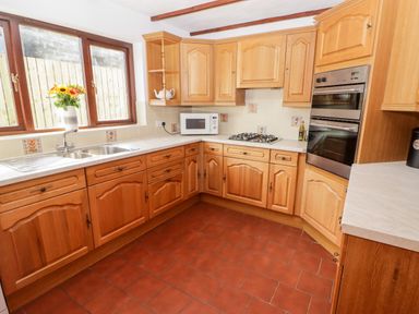 A kitchen with wooden cabinets a double sink a microwave a gas stove and built in ovens at Fountain Folly in Moylgrove near St Dogmaels