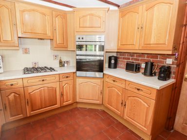 A kitchen with wooden cabinets a gas stove built in oven countertop appliances and tiled floor at Fountain Folly in Moylgrove near St Dogmaels