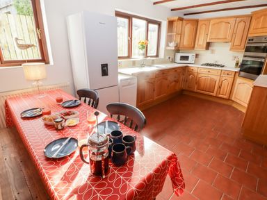 A kitchen with wooden cabinets a refrigerator a dining table with food and drink at Fountain Folly in Moylgrove near St Dogmaels
