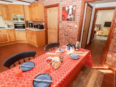 A kitchen with wooden cabinets a red patterned tablecloth on a dining table and plates with croissants and strawberries at Fountain Folly in Moylgrove near St Dogmaels