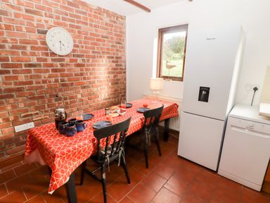 A kitchen with a table covered by a red patterned tablecloth two black chairs a refrigerator and a dishwasher at Fountain Folly in Moylgrove near St Dogmaels