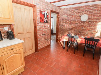 A kitchen with brick walls two black chairs a table with a red tablecloth and wooden cabinets at Fountain Folly Moylgrove near St Dogmaels