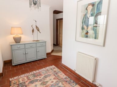 A hallway with a gray cabinet holding a lamp and bird sculptures a radiator on the wall and a framed painting at Fountain Folly in Moylgrove near St Dogmaels