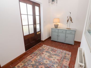 An entryway with double wooden doors a patterned rug a blue cabinet with a lamp and bird sculptures at Fountain Folly Moylgrove near St Dogmaels