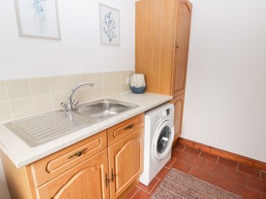 A utility room with a stainless steel sink wooden cabinets a washing machine and two wall pictures at Fountain Folly Moylgrove near St Dogmaels