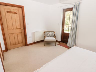 A room with a wooden door a single chair with a cushion a glass-paneled door with striped curtains and a bed partially visible at Fountain Folly in Moylgrove near St Dogmaels