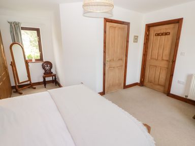 A bedroom with a bed a full length mirror a wooden chair two wooden doors and a window at Fountain Folly in Moylgrove near St Dogmaels