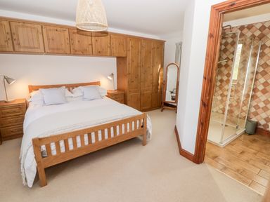 A bedroom with a wooden bed between two side tables and built-in wooden wardrobes with an en suite shower at Fountain Folly Moylgrove near St Dogmaels