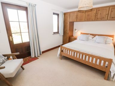 A bedroom with a wooden bed and cabinets a chair and two windows at Fountain Folly Moylgrove near St Dogmaels