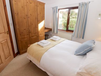 A bedroom with a double bed towels on bed wooden wardrobe and a window with striped curtains at Fountain Folly in Moylgrove near St Dogmaels