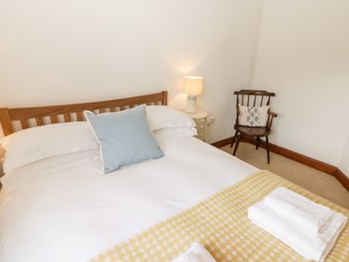 A bedroom with a wooden bed and white linens a bedside table with a lamp and a wooden chair with a cushion at Fountain Folly in Moylgrove near St Dogmaels