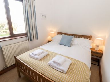 A bedroom with a wooden bed frame two bedside tables with lamps window with striped curtains and towels on the bed at Fountain Folly in Moylgrove near St Dogmaels